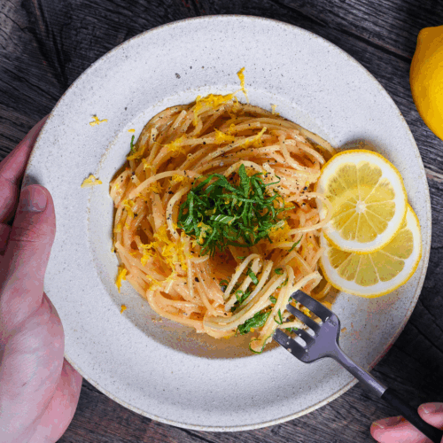 Mentaiko Pasta topped with shredded perilla leaves and lemon zest with a hand holding a fork with some pasta twirls around it
