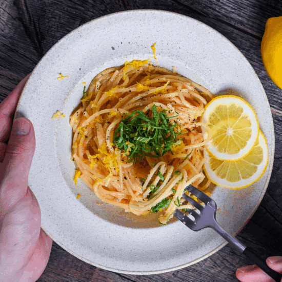 Mentaiko Pasta topped with shredded perilla leaves and lemon zest with a hand holding a fork with some pasta twirls around it
