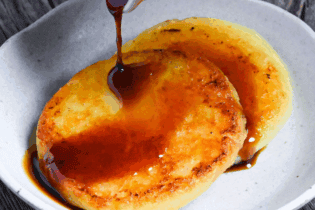 pouring sauce over two potato mochi on a small white plate