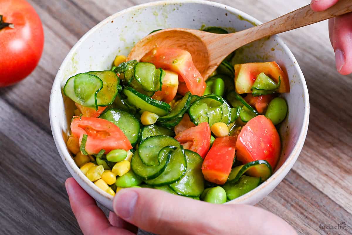a bowl filled with summer vegetable salad and shiso dressing with a wooden spoon