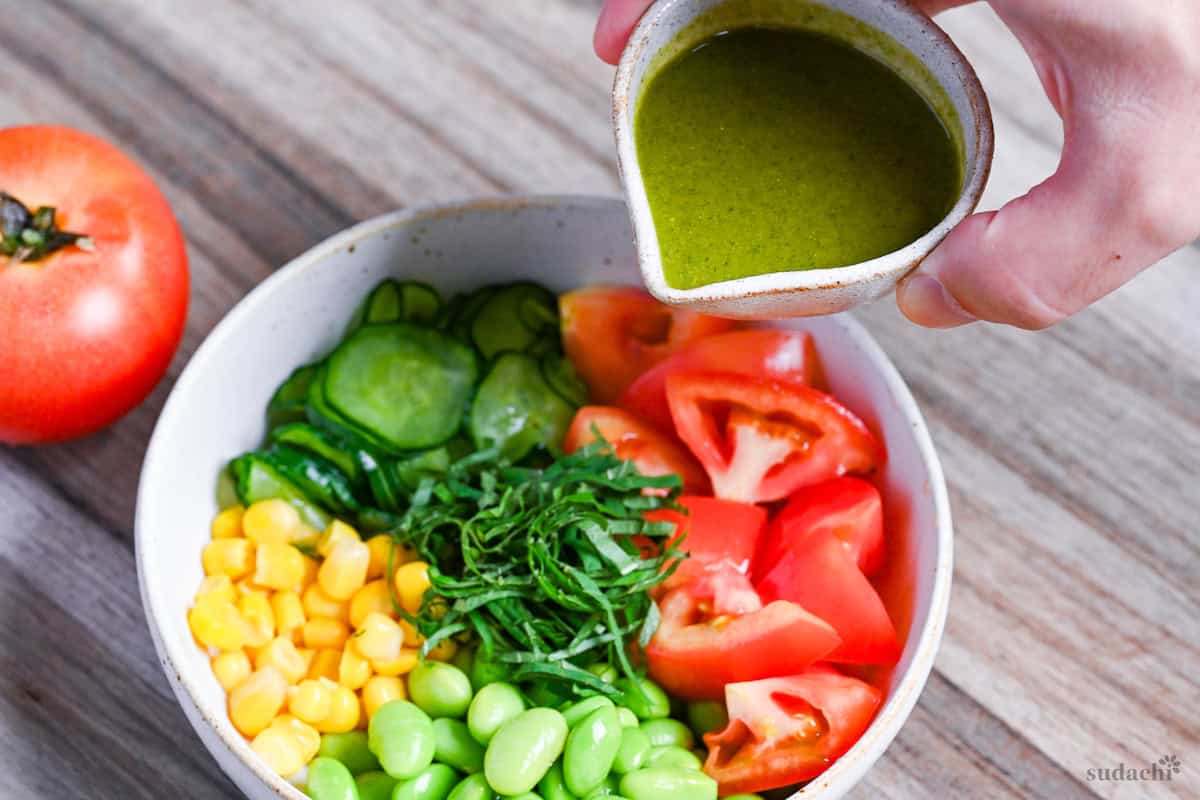 a small jug of shiso dressing being held above a summer vegetable salad