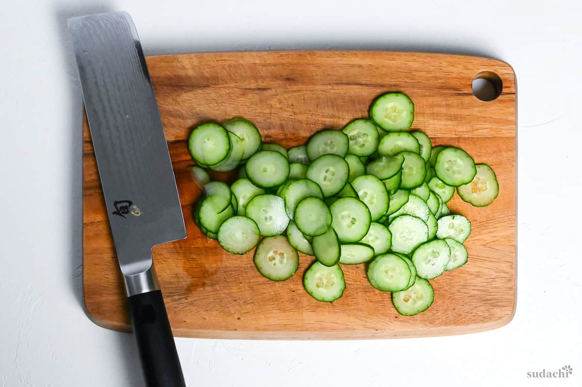 sliced cucumber on a wooden cutting board with vegetable knife
