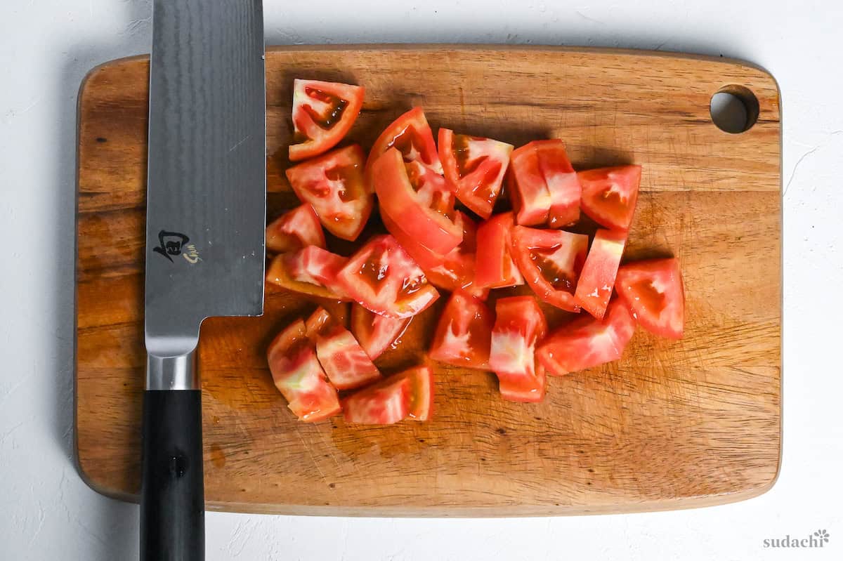 roughly cut tomato on a wooden cutting board with a vegetable knife