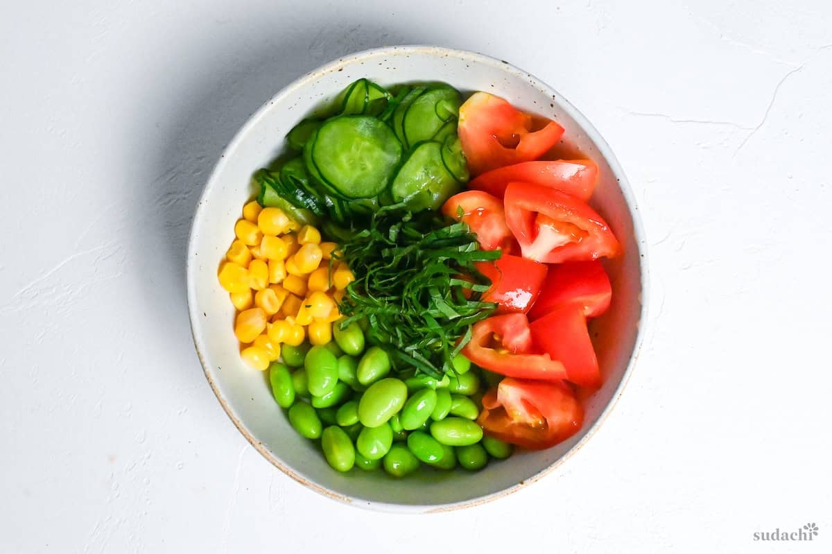 summer shiso salad made with cucumber, tomatoes, edamame, corn and shredded shiso in an off-white mottled bowl