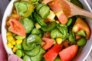 a hand holding a bowl filled with summer vegetable salad and shiso dressing with a wooden spoon close up