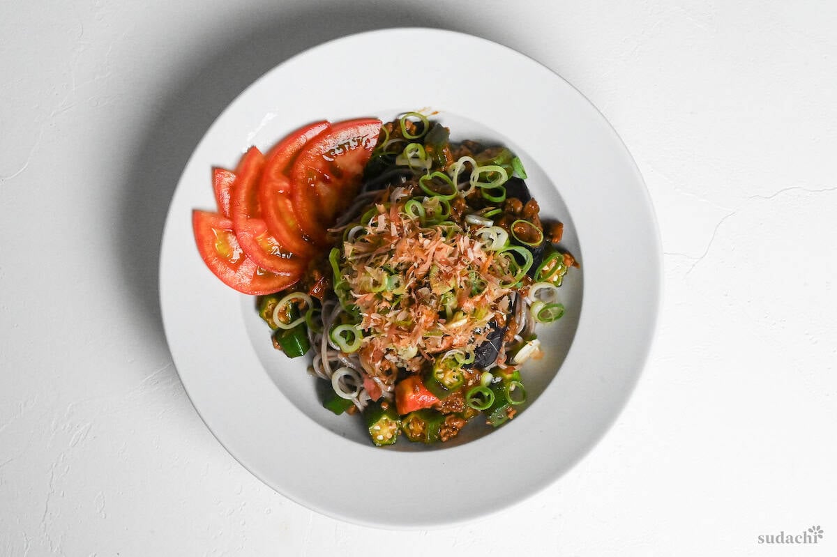 Summer soba in a white dish topped with chopped green onions, bonito flakes and sliced tomatoes