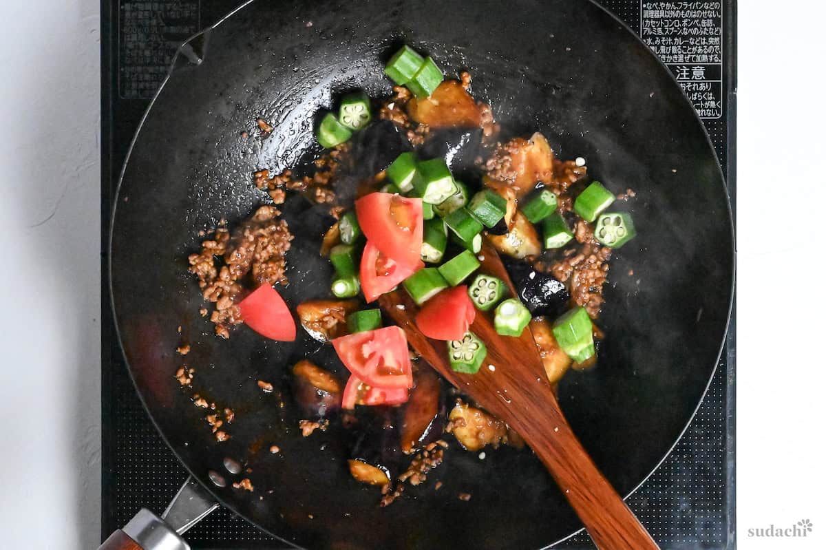 tomato and okra added to ground pork and eggplant pieces in a wok