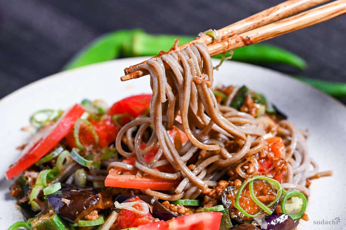 Wooden chopsticks holding up soba noodles from summer soba with miso meat sauce
