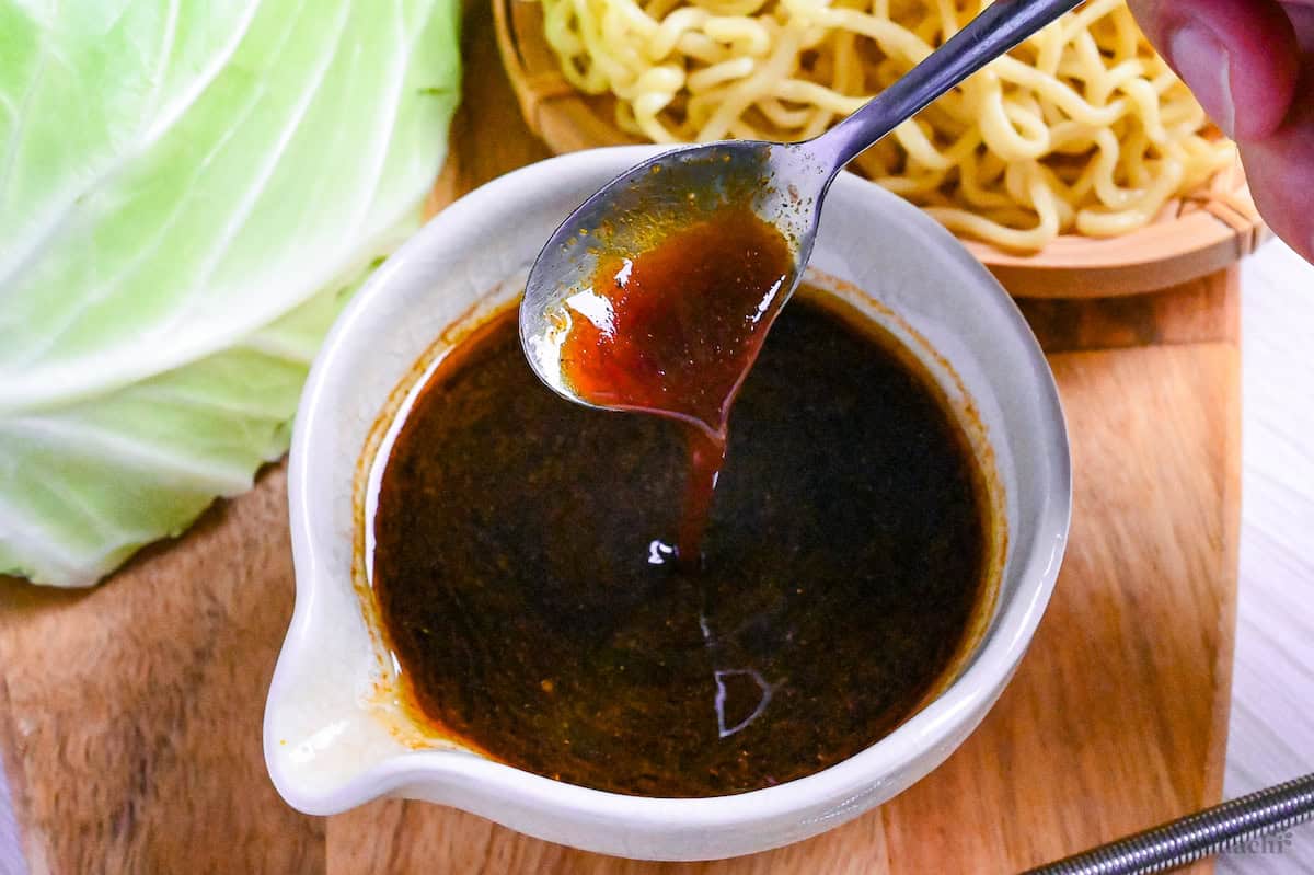 a spoon pouring homemade yakisoba sauce into a small jug on a wooden board