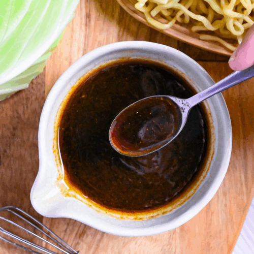 Homemade yakisoba sauce in a small white ceramic jug with silver spoon held above