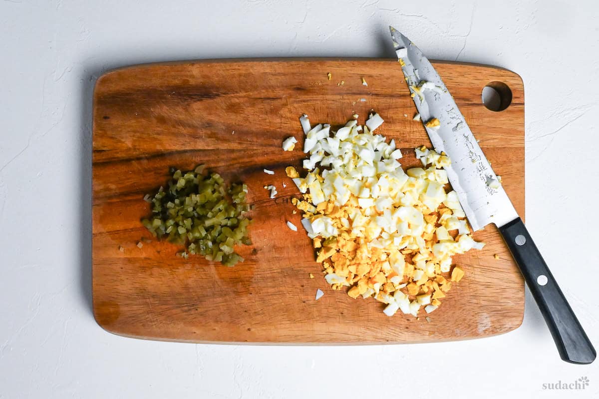 finely diced pickled gherkin and boiled egg on a wooden cutting board with knife