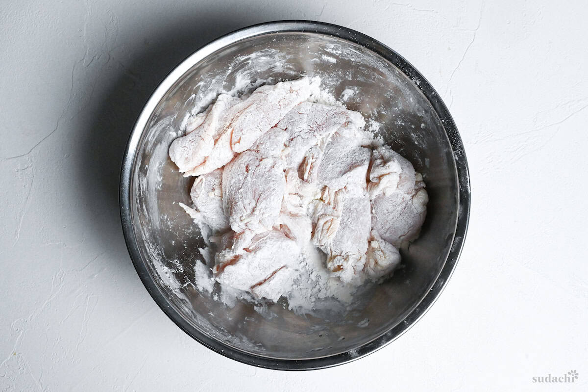 chicken breast pieces coated with starch in a metal mixing bowl