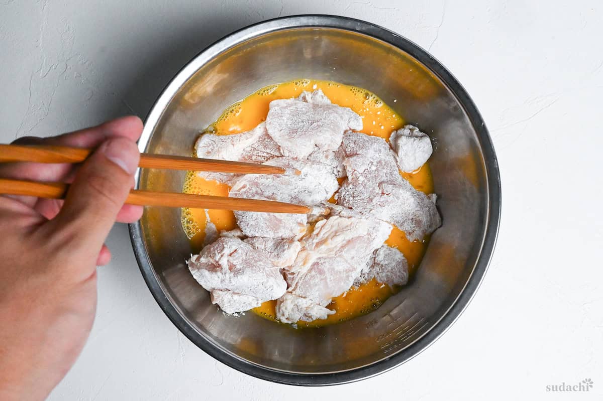 starch coated chicken breast pieces in mixing bowl with whisked egg