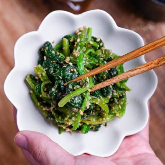 Japanese Sesame Spinach Salad (Horenso Goma Ae) in a white bowl in a hand with wooden chopsticks