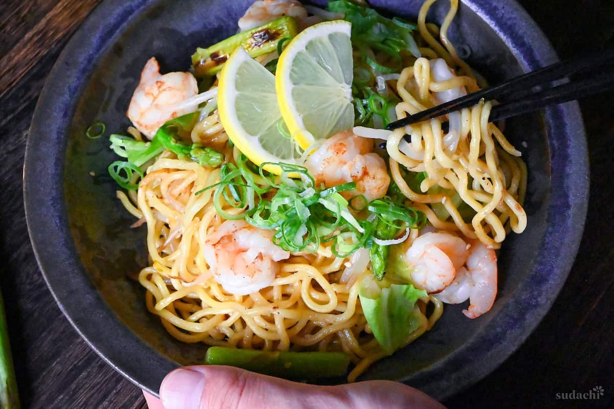 Shio Lemon Yakisoba in a blue/black iridescent bowl being lifted with black chopsticks