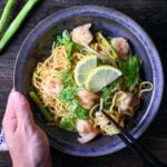 Shio Lemon Yakisoba in a blue/black iridescent bowl held with a hand and black chopsticks lifting noodles top down view