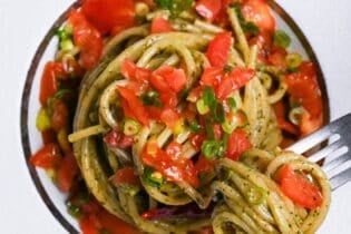 Japanese shiso pesto pasta topped with marinated tomato in a white pasta dish with silver fork top down