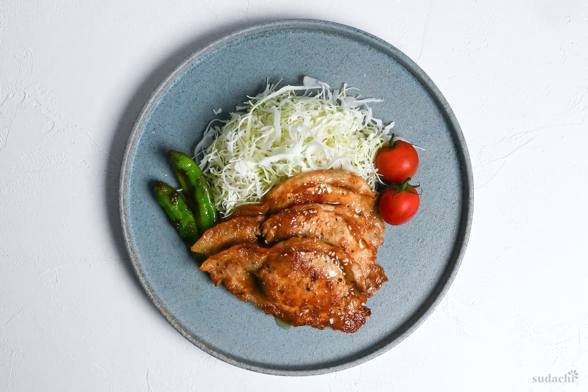 Final plating of shogayaki (Japanese ginger pork) with charred shishito peppers, shredded cabbage and mini tomatoes
