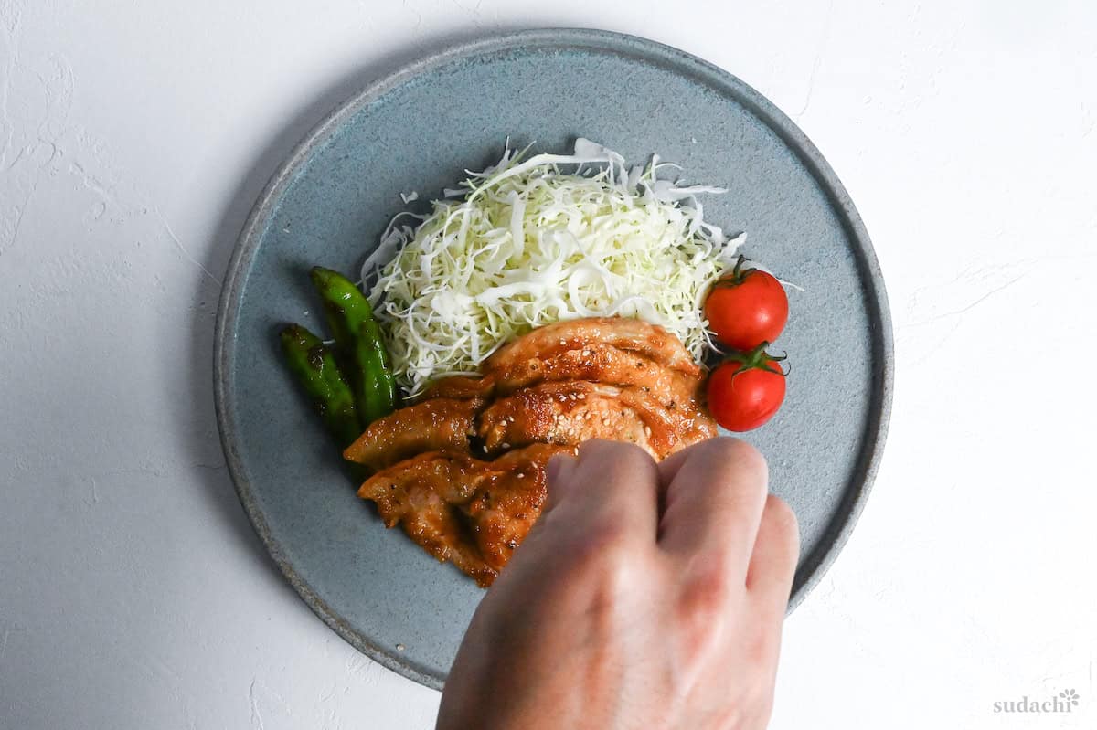 A hand sprinkling Japanese ginger pork with toasted sesame seeds
