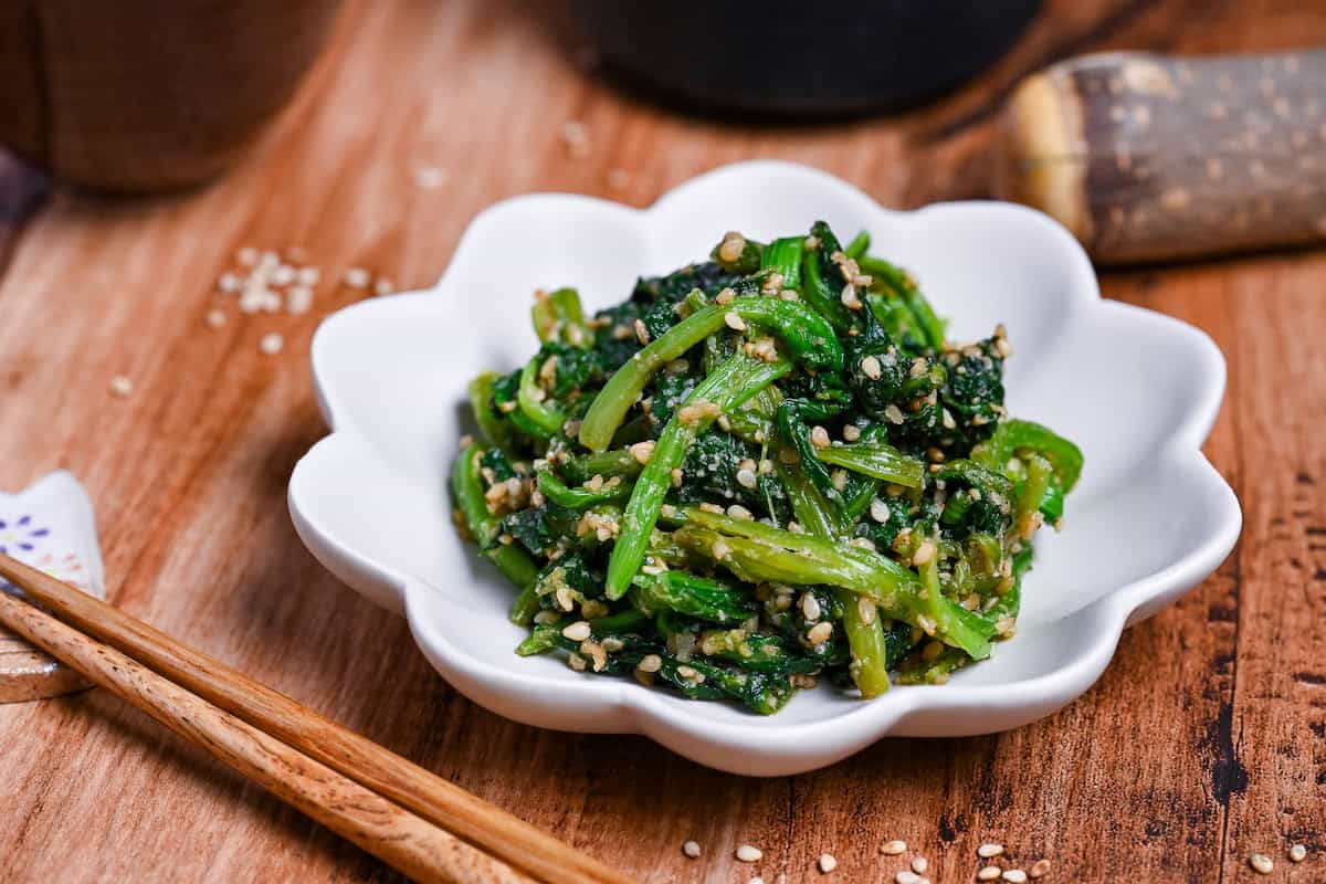 Close up of Japanese Sesame Spinach Salad (Horenso Goma Ae) in a small flower shaped white bowl on a wooden surface