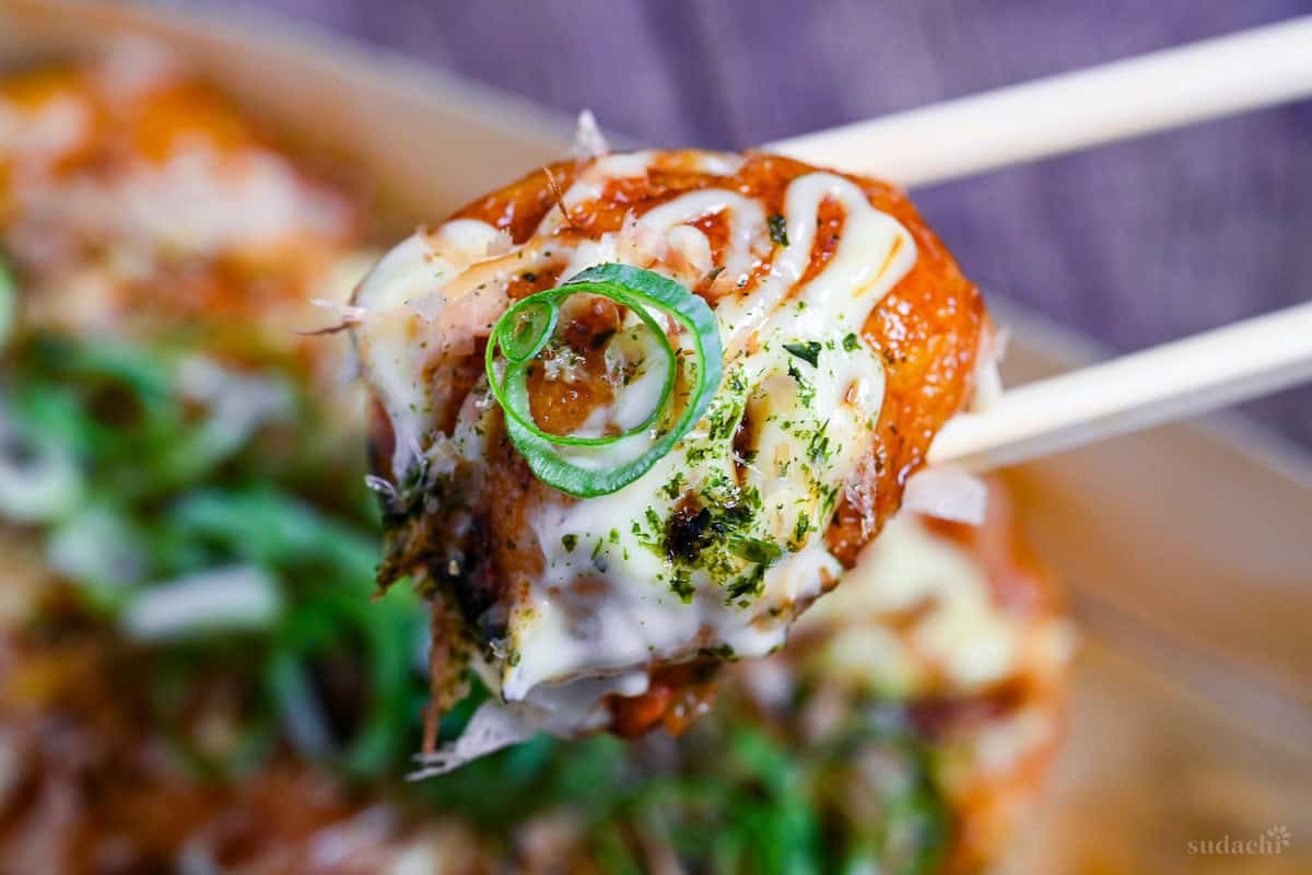 close up of homemade takoyaki held up by wooden chopsticks