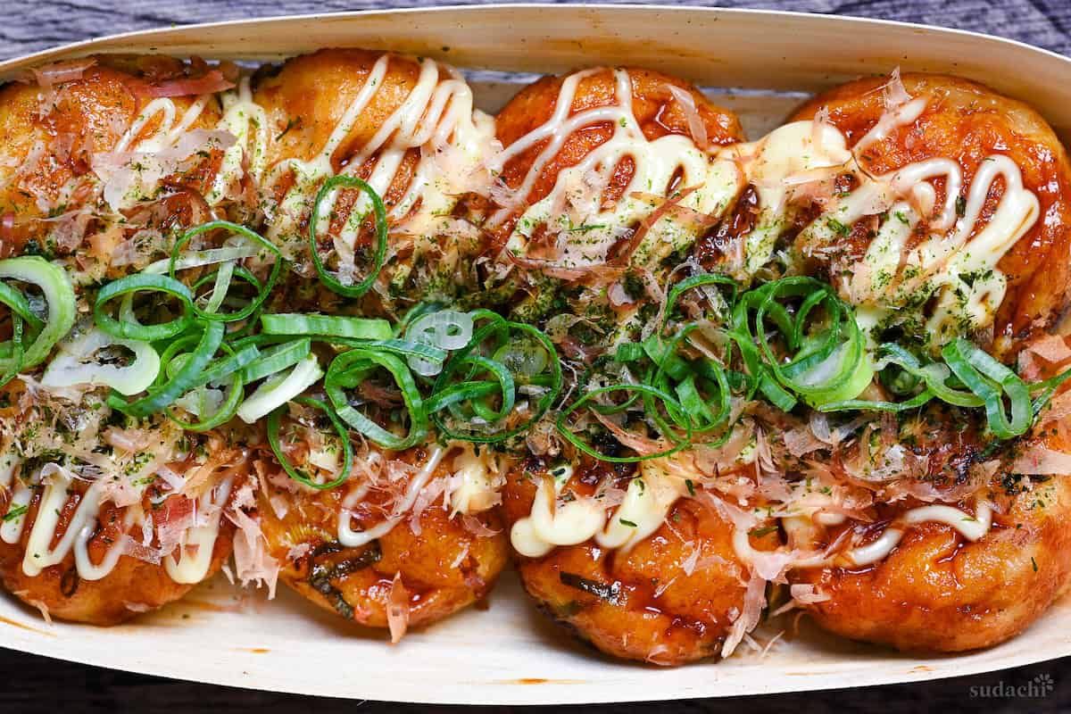 8 homemade takoyaki topped with takoyaki sauce, mayonnaise, bonito flakes, aonori and chopped green onions served in a bamboo boat top down