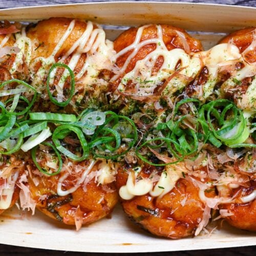 8 homemade takoyaki topped with takoyaki sauce, mayonnaise, bonito flakes, aonori and chopped green onions served in a bamboo boat top down