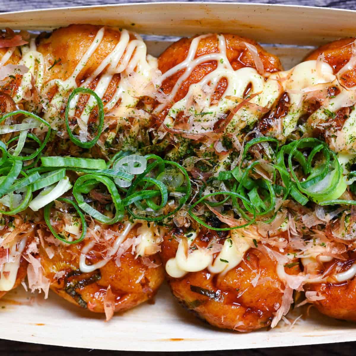 8 homemade takoyaki topped with takoyaki sauce, mayonnaise, bonito flakes, aonori and chopped green onions served in a bamboo boat top down