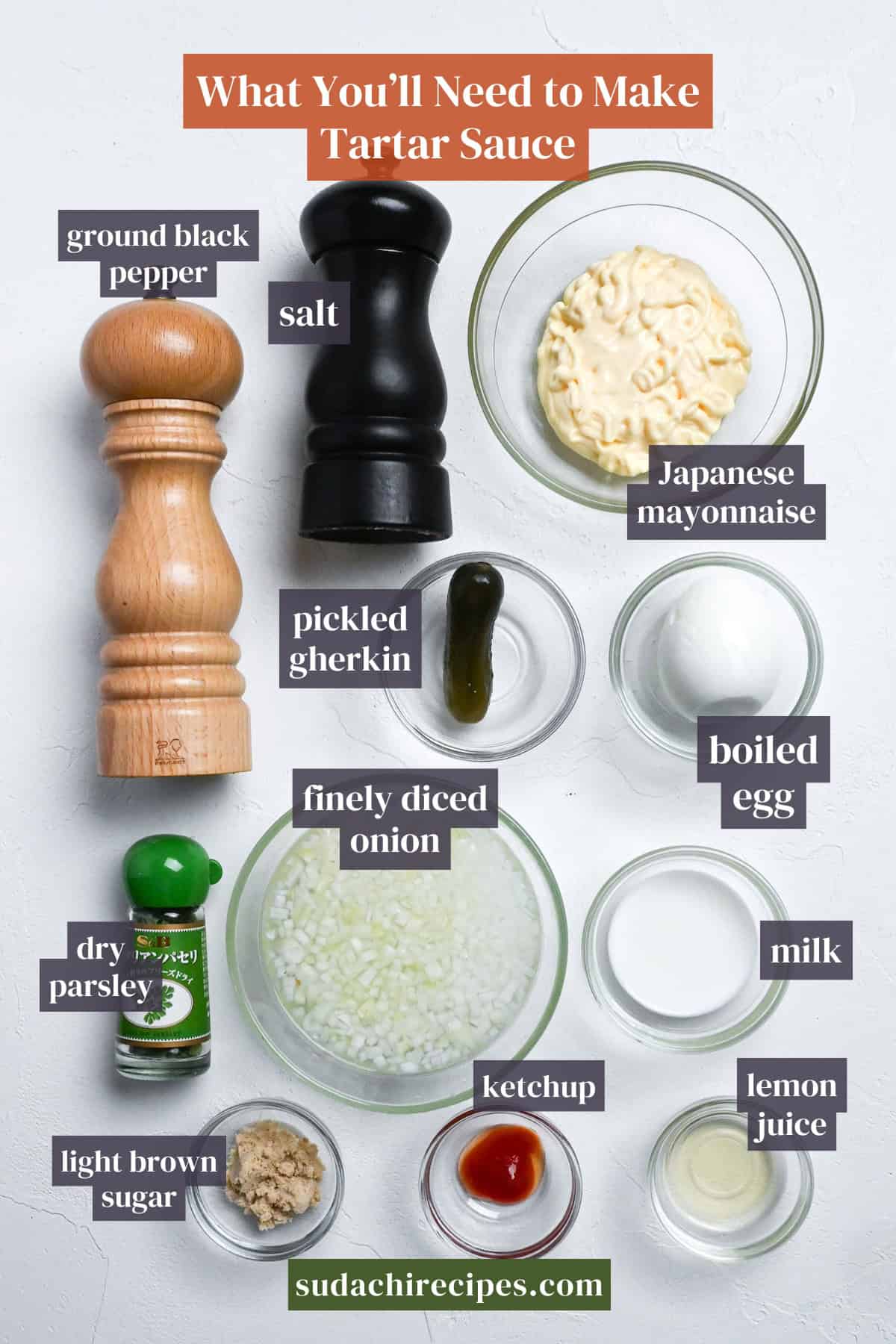 Ingredients needed to make tartar sauce. From top to bottom, left to right: ground black pepper and salt in wooden grinders, Japanese mayo, pickled gherkin, boiled egg, finely diced onion, dry parsley, milk, light brown sugar, ketchup, lemon juice