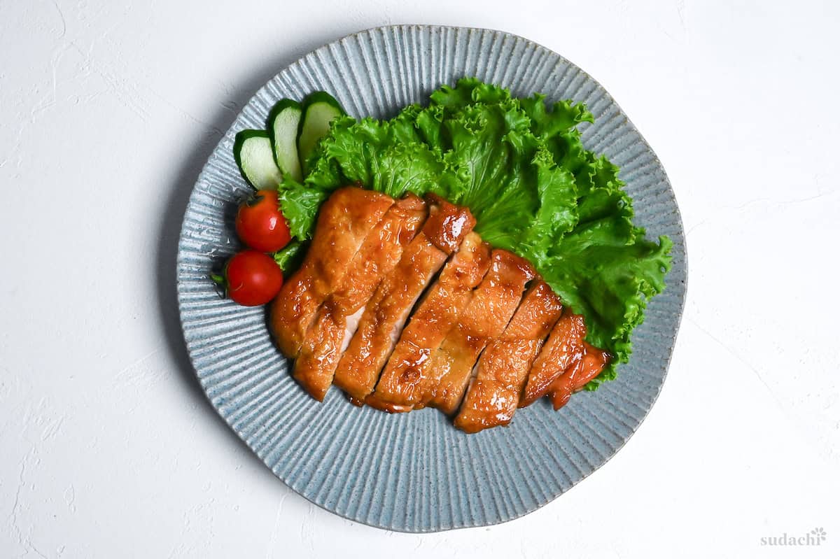 Teriyaki chicken on a blue plate with frilly lettuce, cucumber and tomatoes