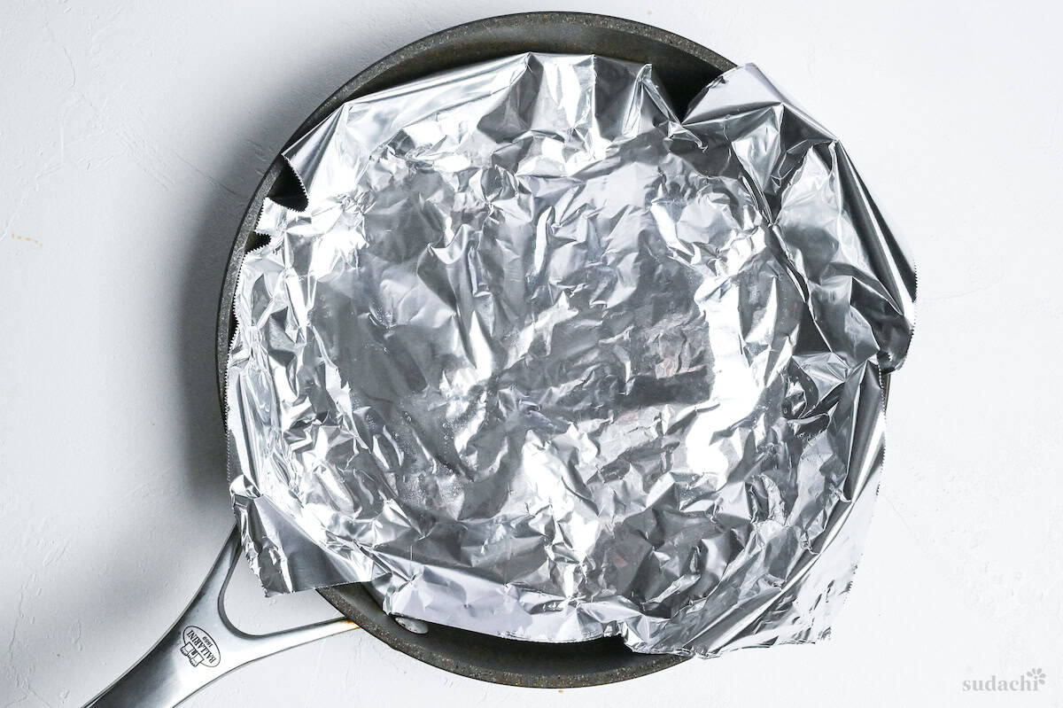 chicken thighs covered with foil in a cold pan on a white surface