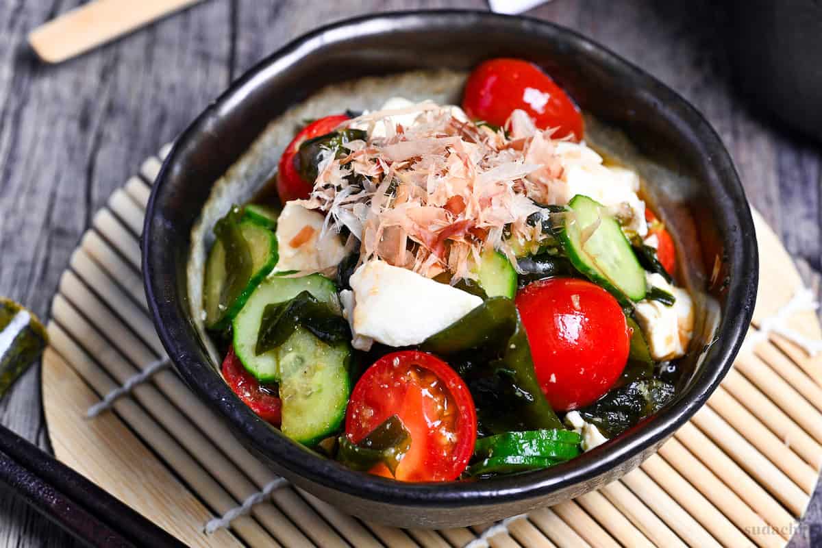 Japanese wakame salad made with wakame seaweed, mini tomatoes, cucumber and silken tofu served in a mottled gray bowl with dark brown edge