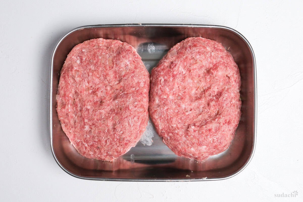 two raw hamburg patties in a steel container