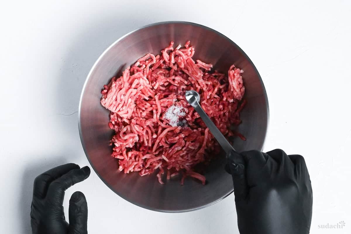 seasoning ground meat with salt in a mixing bowl