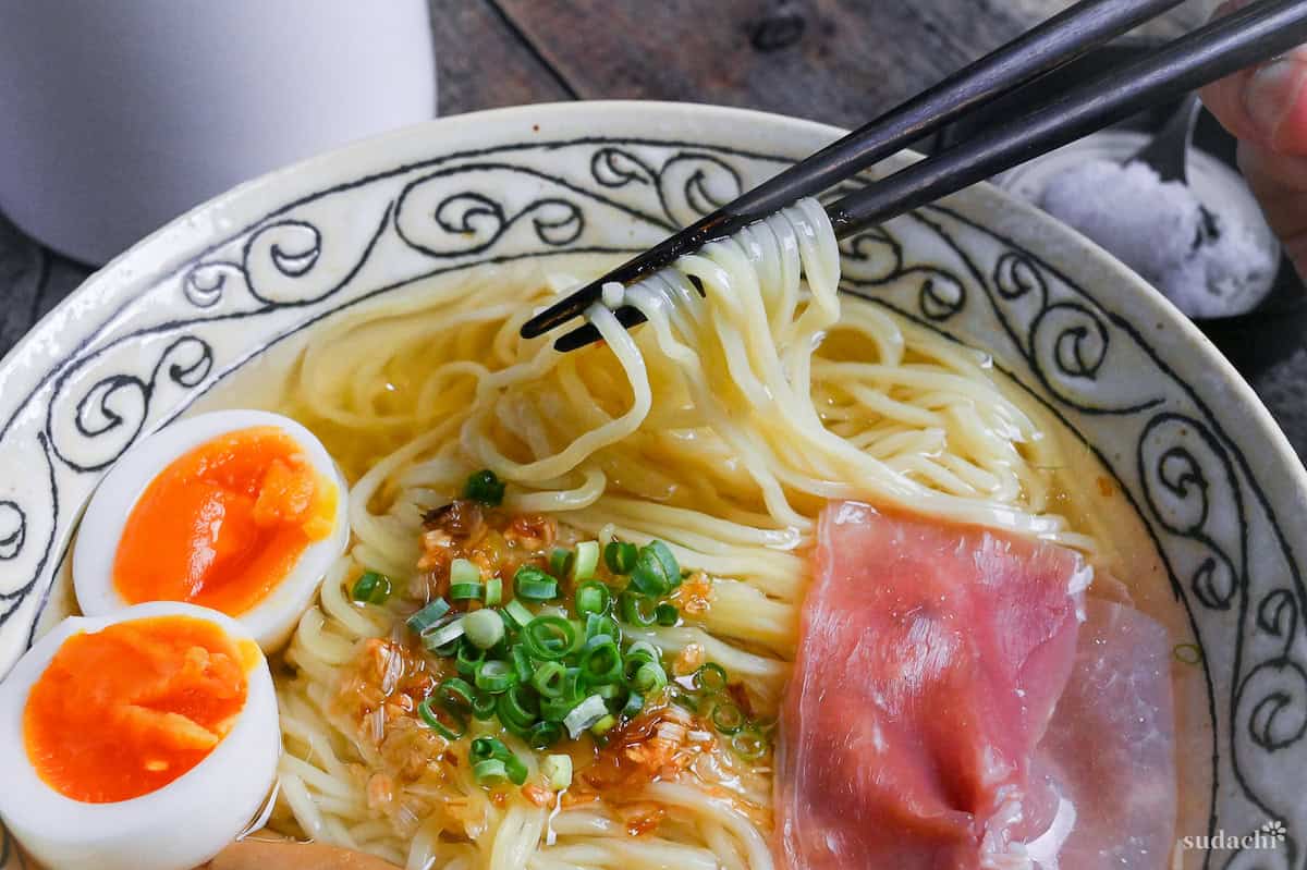 close up of shio ramen held up with black chopsticks