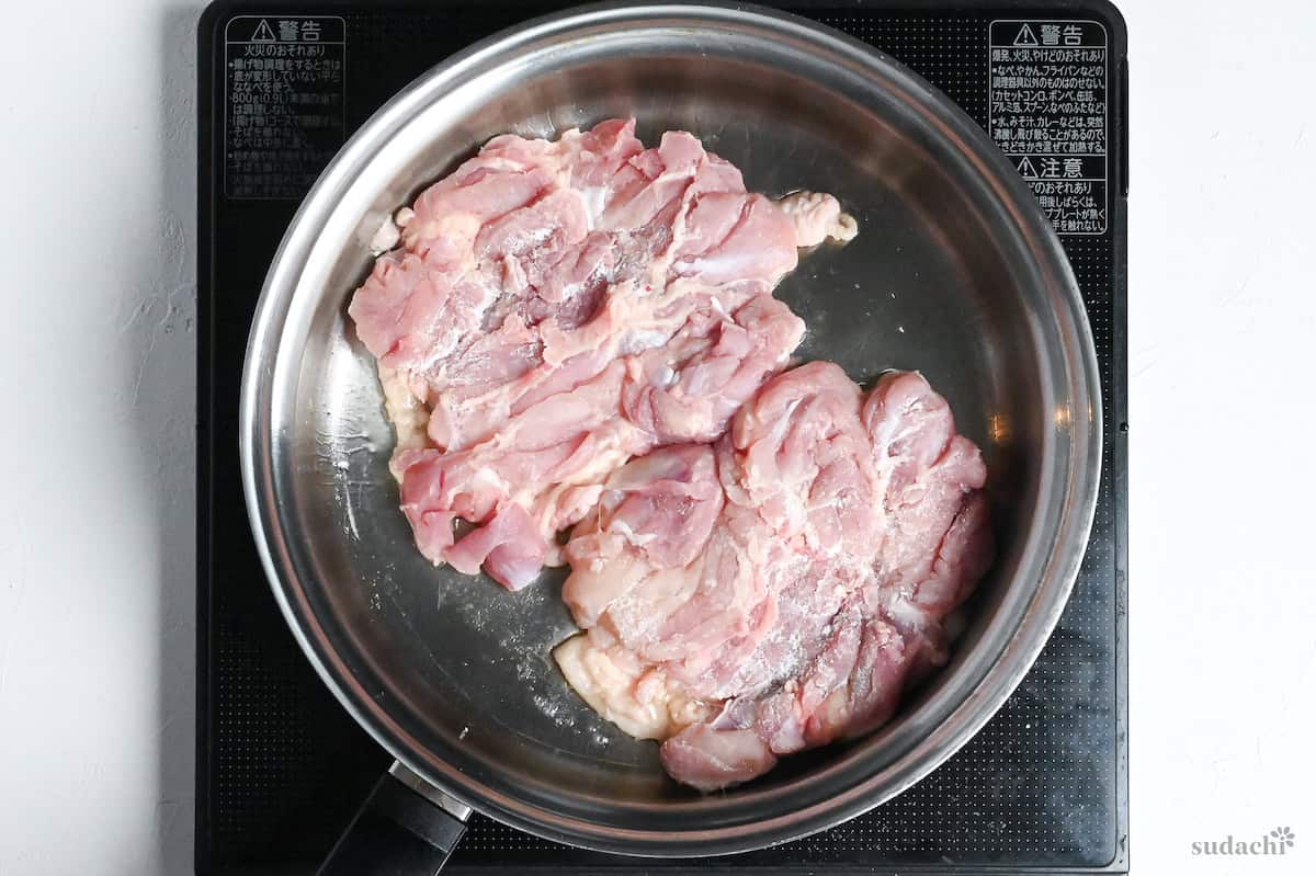 Two boneless chicken thighs skin-side down in a stainless steel pan on the stovetop