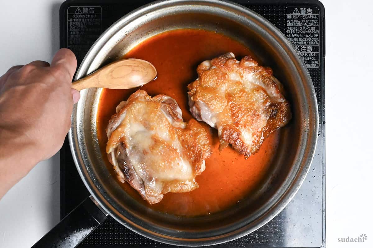using a wooden spoon to baste chicken thighs with teriyaki sauce