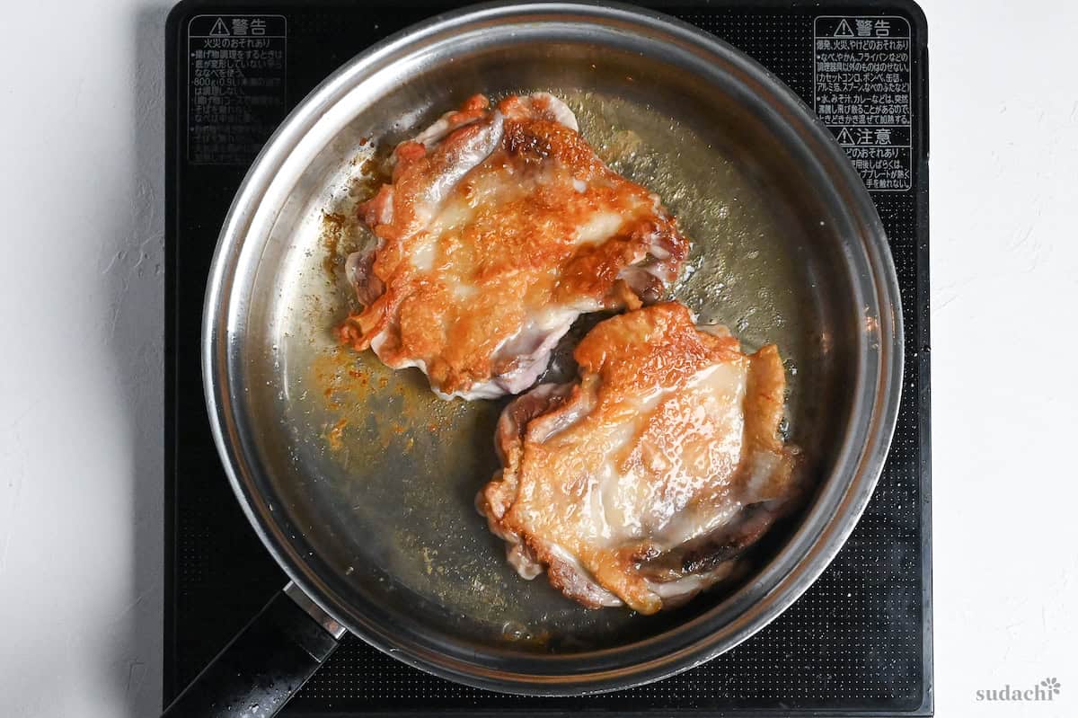 Two boneless chicken thighs frying in a stainless steel pan