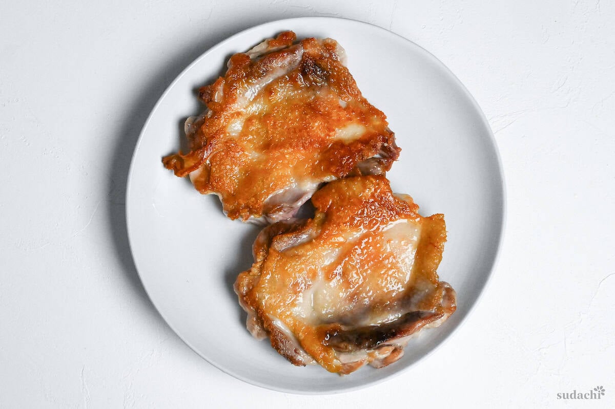 two pan-fried boneless chicken thighs resting on a white plate