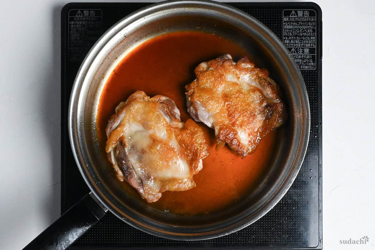two fried boneless chicken thighs in a stainless steel pan with teriyaki sauce
