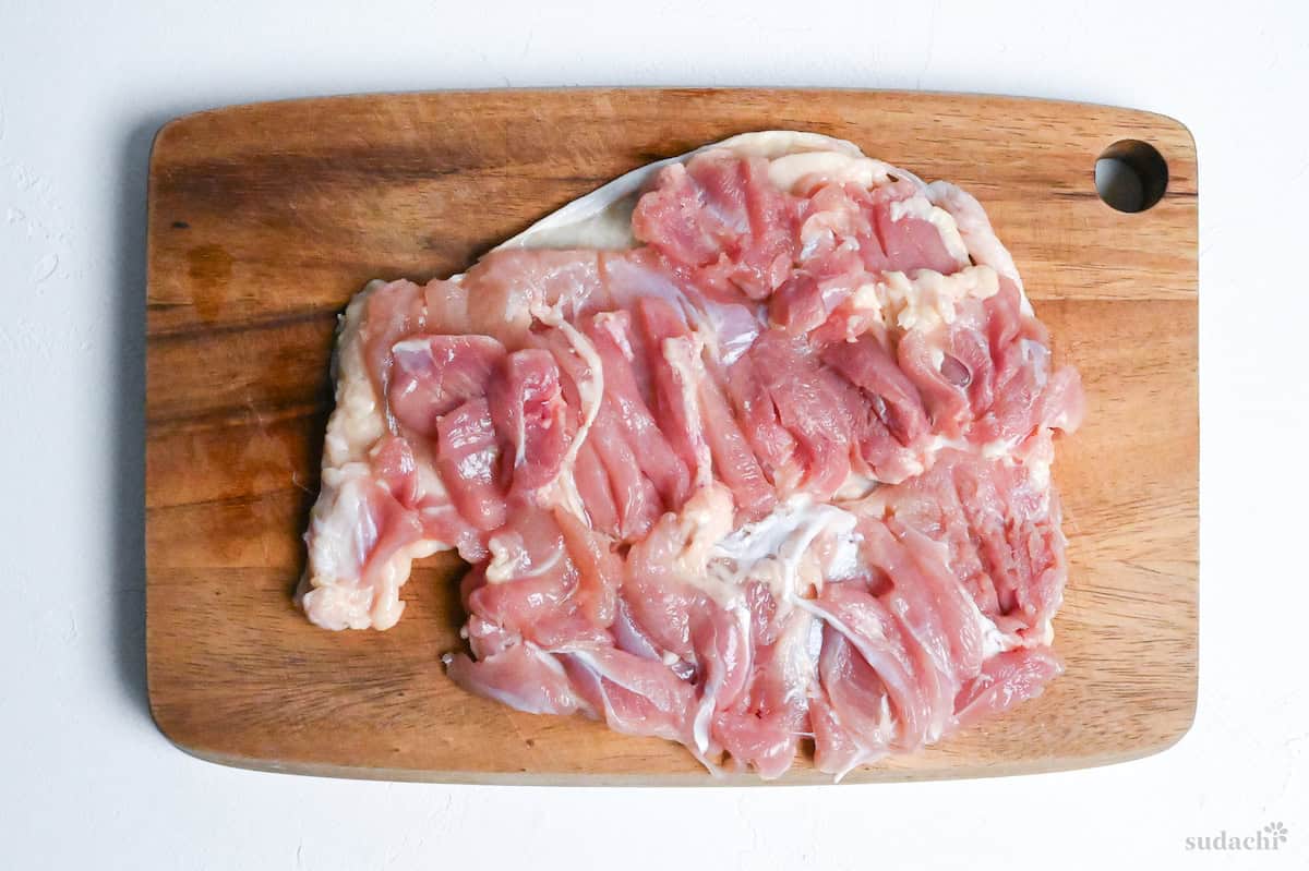 scored chicken thigh on a wooden cutting board