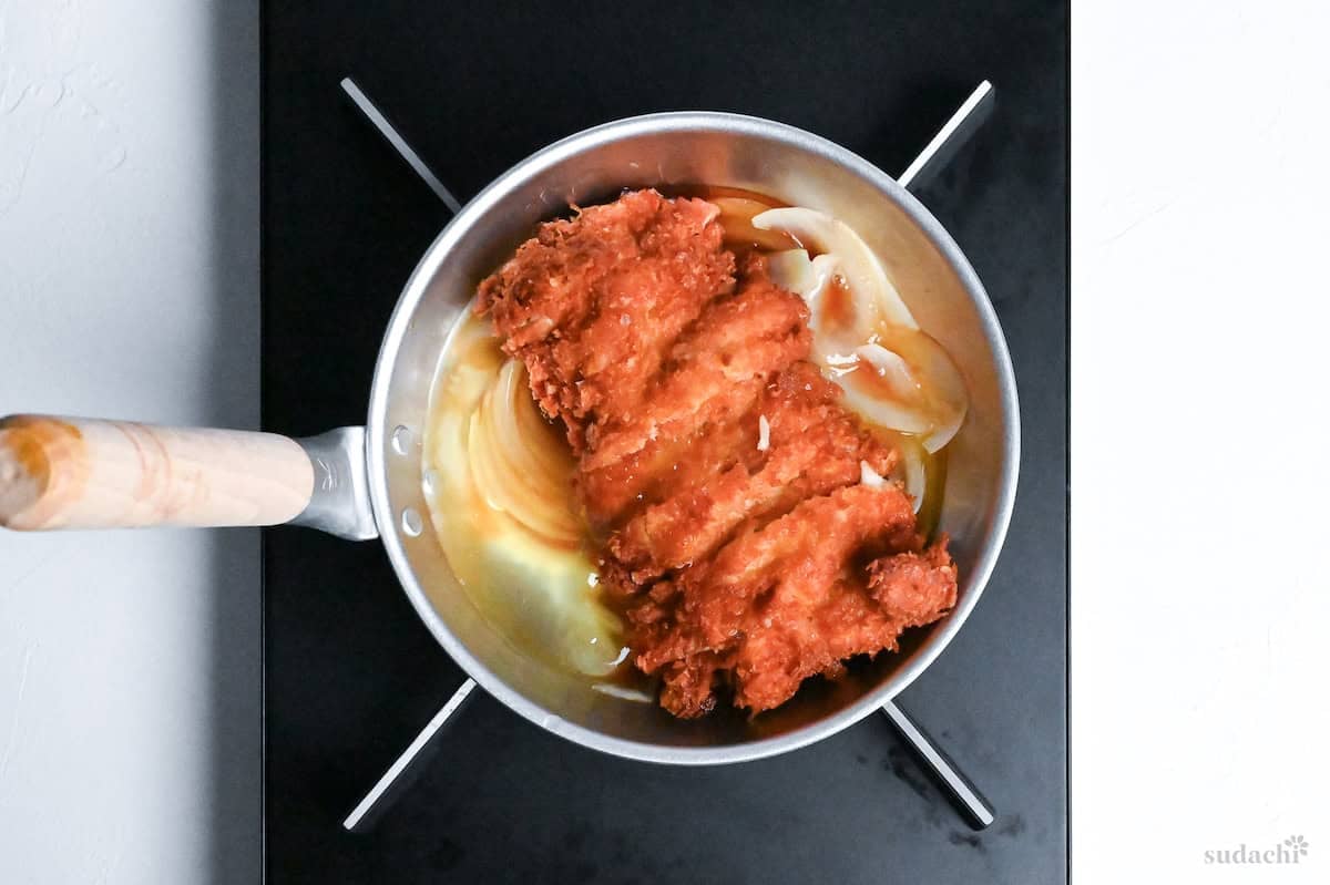 sliced chicken cutlet in a pan with dashi and onions