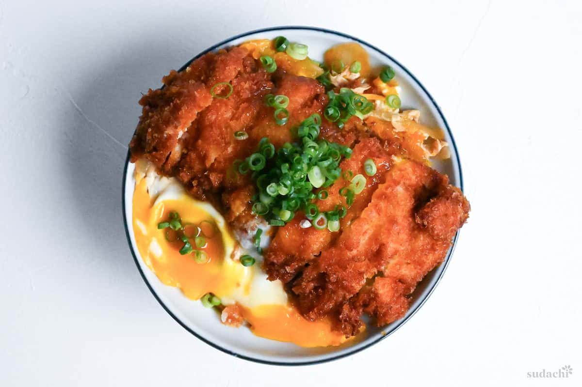 Complete chicken katsudon topped with finely chopped green onions in a white bowl with blue rim