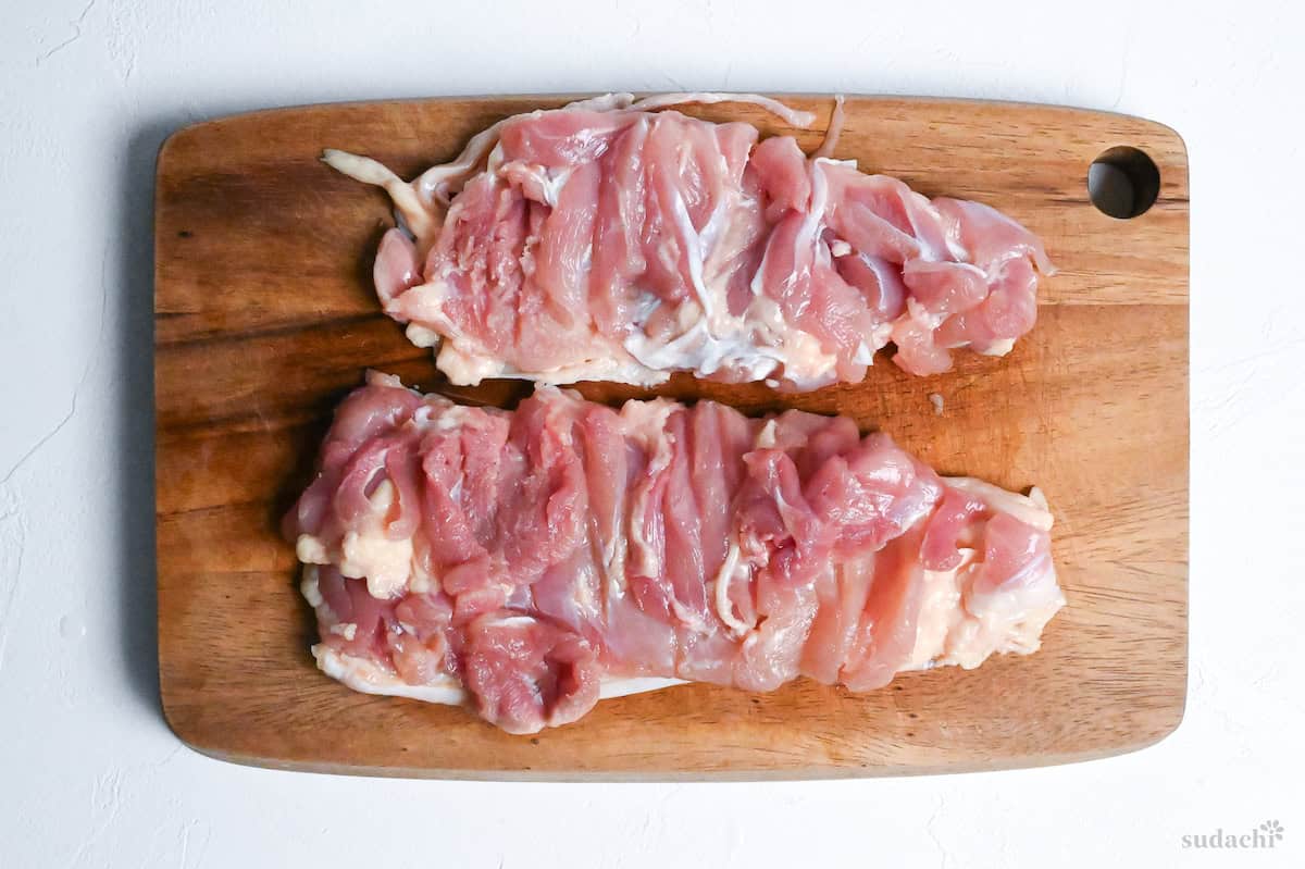 chicken thigh cut in two on a wooden cutting board