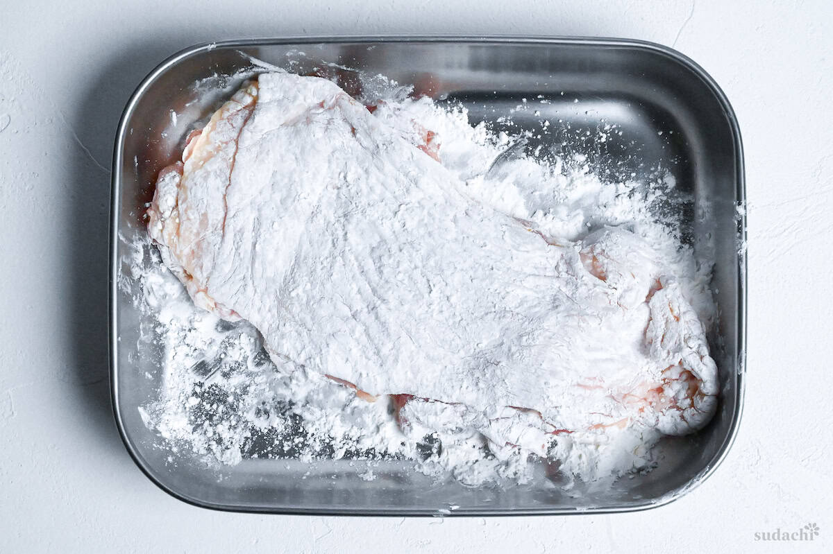 chicken thigh coated with cornstarch in a steel rectangular container