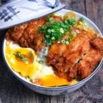 Chicken katsudon in a white and blue bowl with lid resting on the side