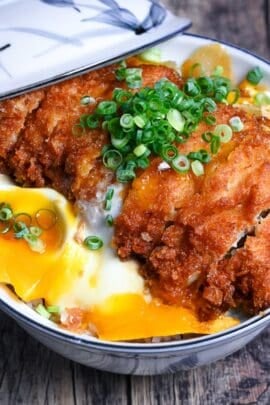 Chicken katsudon in a white and blue bowl with lid resting on the side