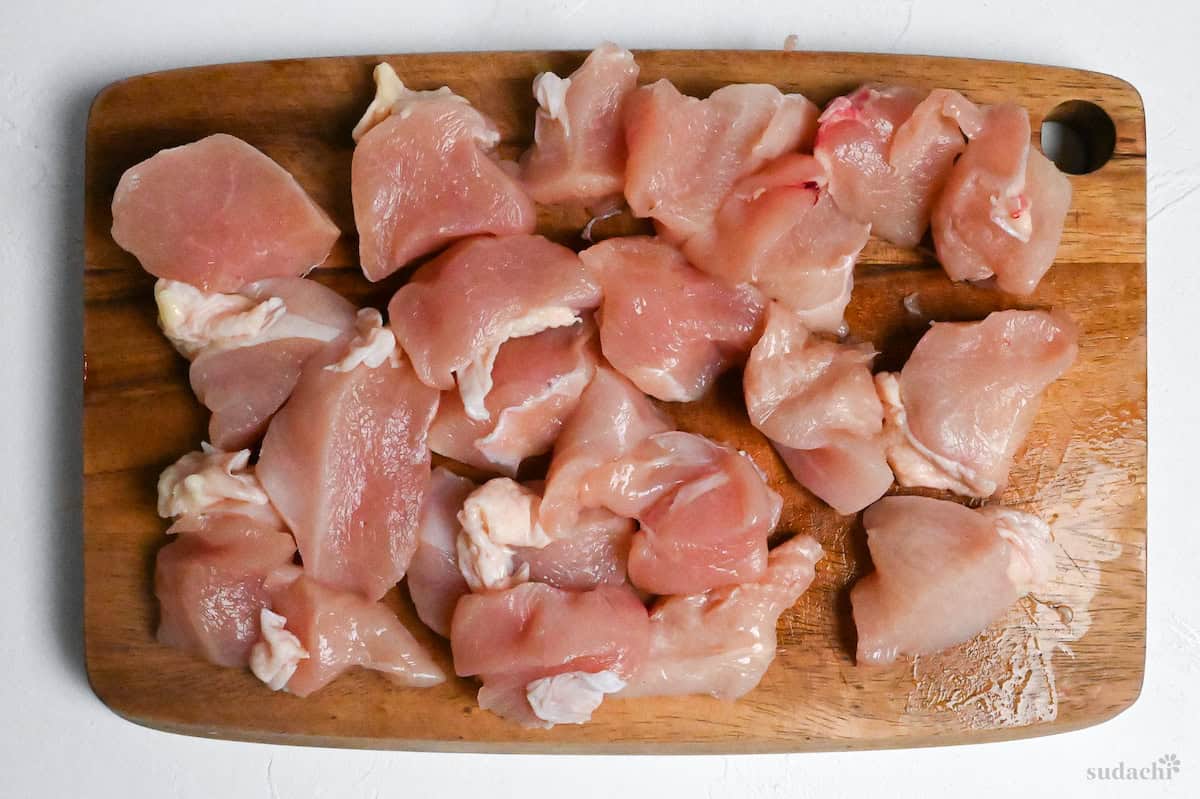 Chicken breast cut into large bitesize pieces against the grain on a wooden cutting board
