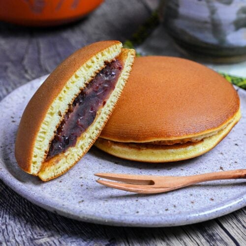 Half a dorayaki pancake revealing tsubuan (chunky red bean paste) in the center resting on a whole dorayaki on a mottled plate