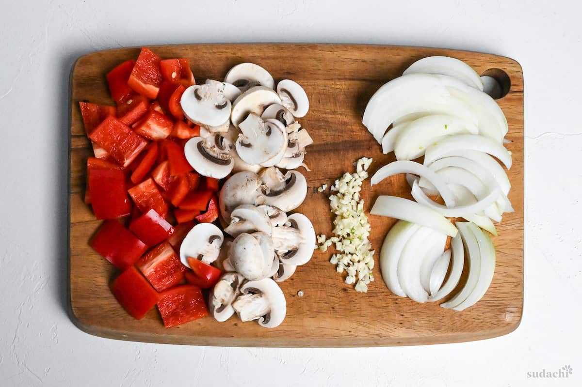 bell peppers, button mushrooms, garlic and onion cut on a wooden cutting board
